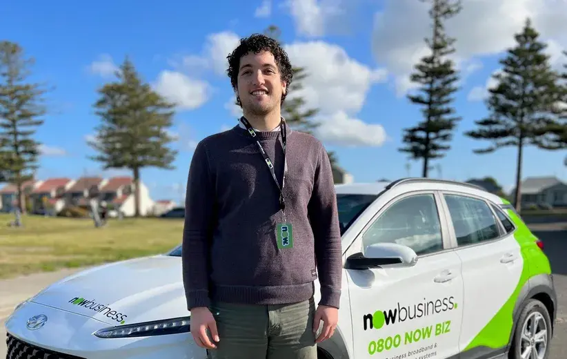Male Now NZ employee standing in front of a company-branded car with Now NZ logo and contact details, emphasizing secure and swift switching services for medium-sized businesses.