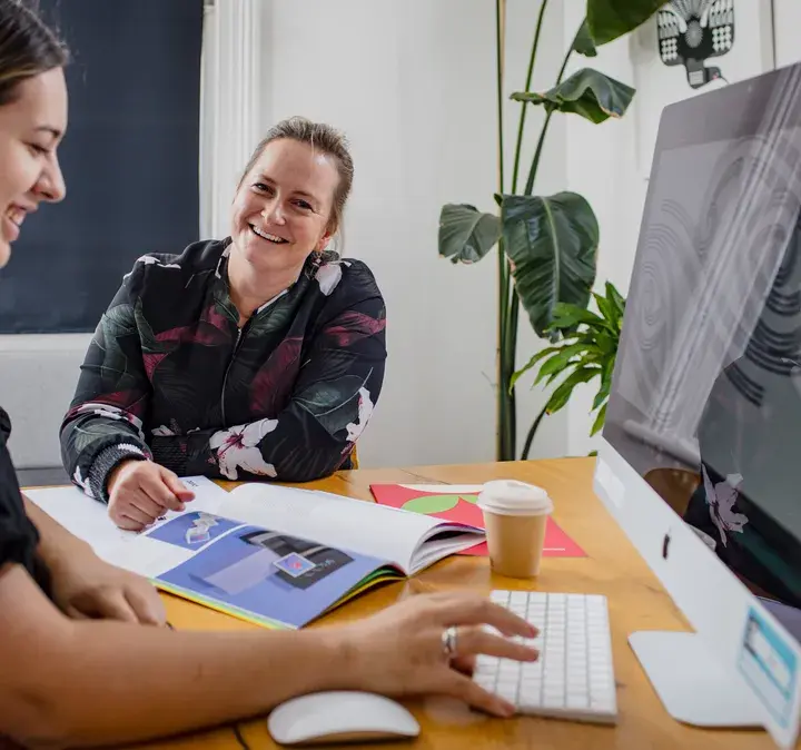 Two women smiling and working on a computer, representing the seamless communication and integration offered by Now's MS Teams Calling