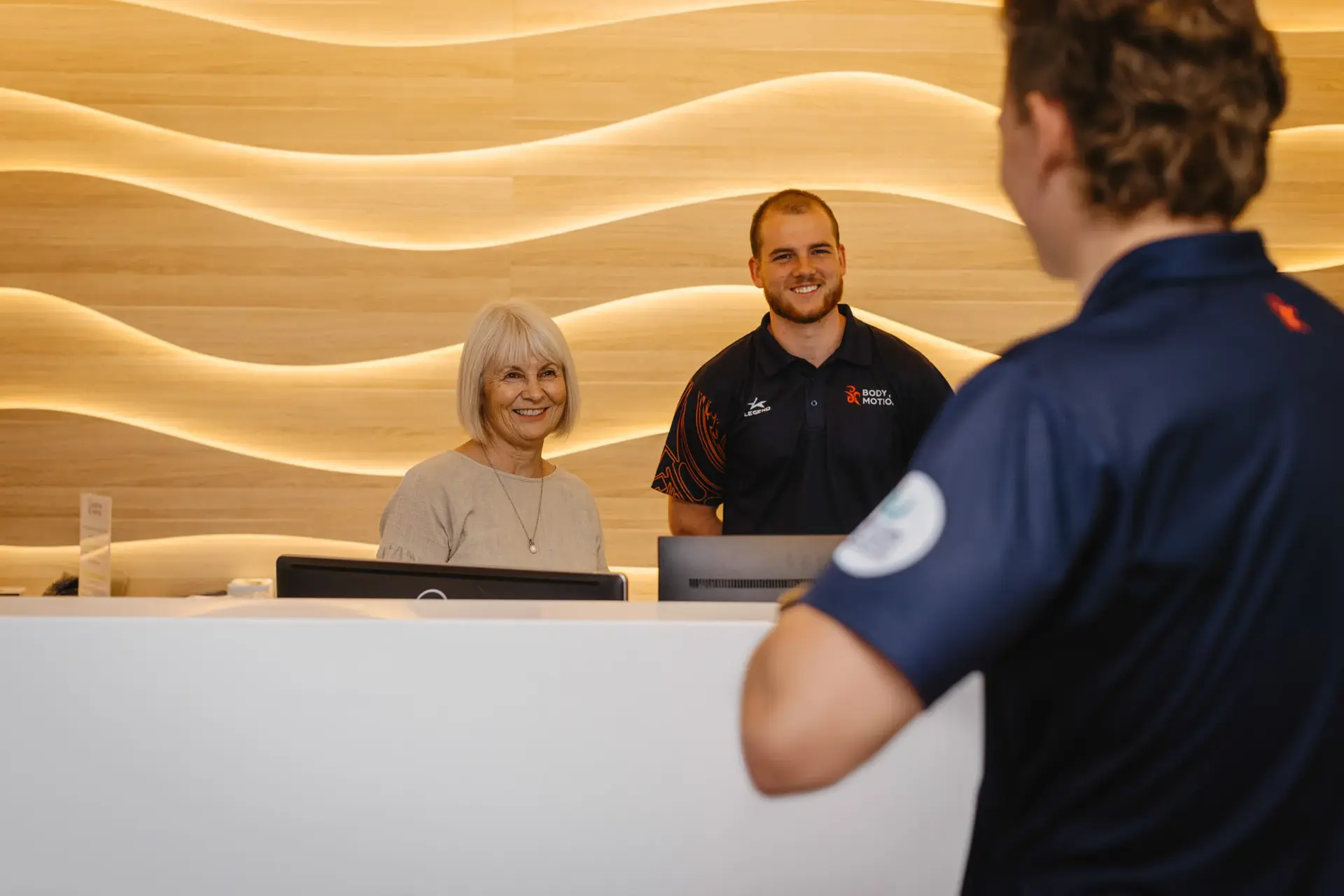 Two Body in Motion staff members smile behind a reception desk, highlighting their partnership with Now Business for reliable phone solutions.