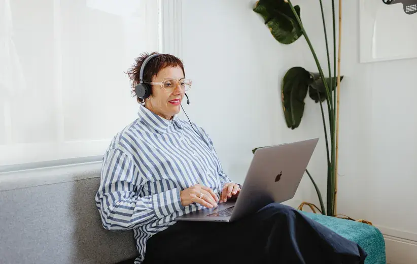Smiling woman using a laptop and headset, representing the bespoke features of Now Reach that optimise work across various industries
