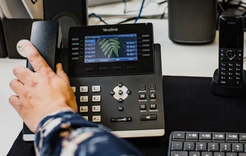 Close-up of a hand using a Yealink office phone with a digital display, highlighting Now NZ's cost-effective and high-quality telecommunications solutions.